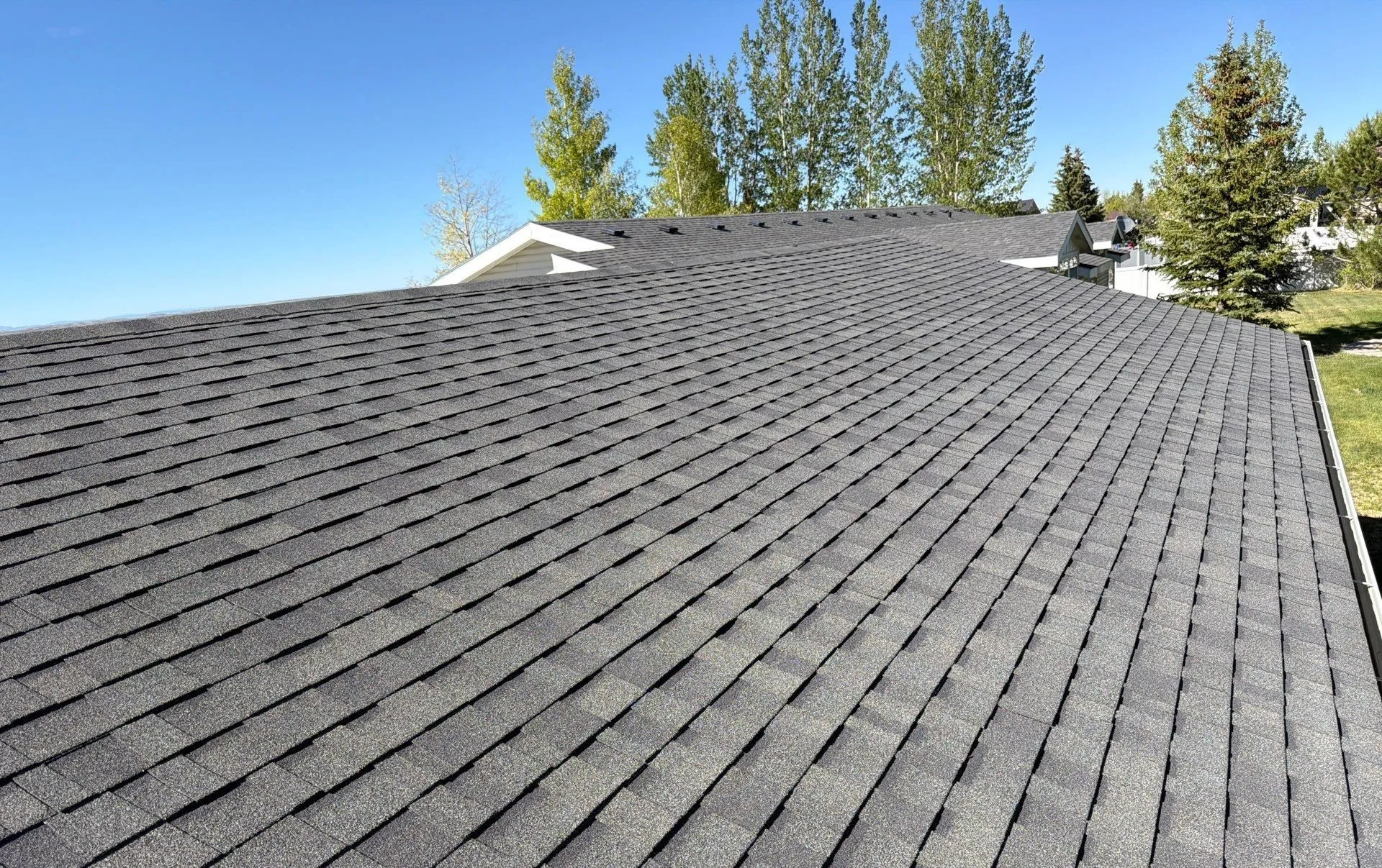 A finished charcoal architectural-shingle roof installed by the Gregco crew under a clear blue sky